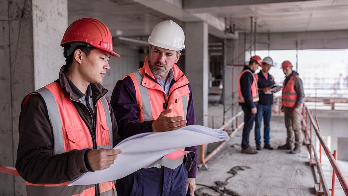 Asian construction worker and European site supervisor reviewing site readiness